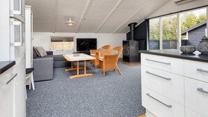 A modern kitchen with white cabinets and a black stove, a dining area with a table and chairs, and a large window providing a view of the outdoors. - 4 Star Holiday Home in Ansager (Ansager)