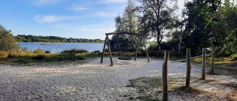 Zona de playa arenosa con un columpio y una cerca de madera.
