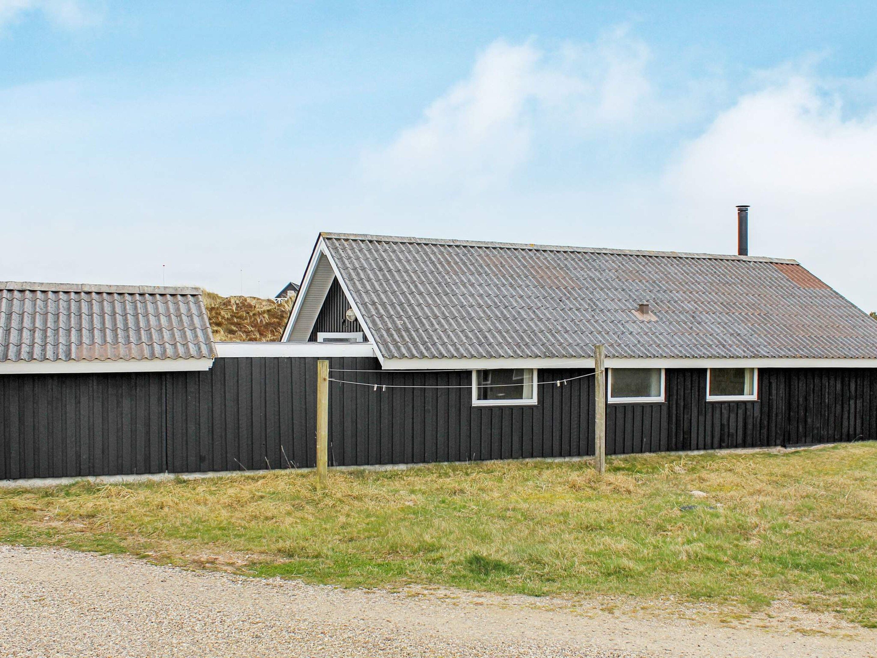 A building with a corrugated metal roof, a wooden fence, and a gravel driveway.