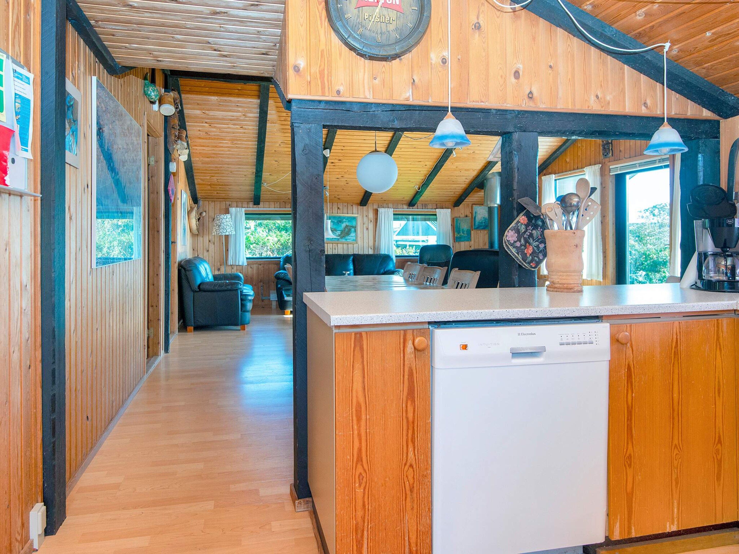 A wooden interior with a kitchen area featuring a dishwasher, a dining table, and a clock on the wall.