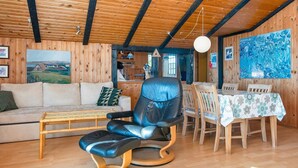 A cozy cabin interior with a wooden ceiling, a sofa, a leather chair, a dining table with chairs, and a painting on the wall. - Serene Holiday Home in Lemvig near Sea (Lemvig)