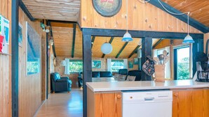 A wooden interior with a kitchen area, wooden ceiling beams, and a dining area with chairs and a table. - Serene Holiday Home in Lemvig near Sea (Lemvig)