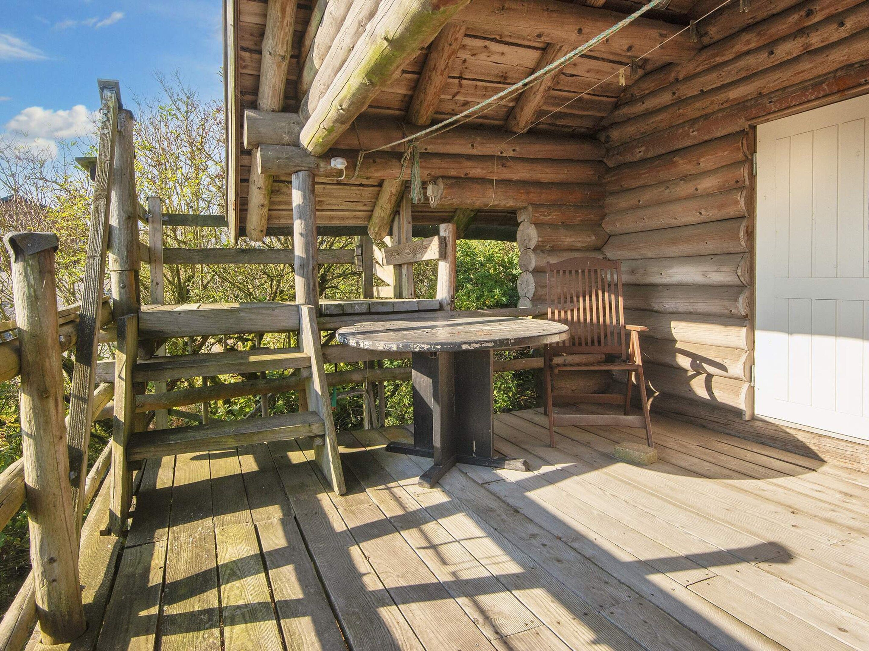 En træhytte med veranda, et bord og en stol.