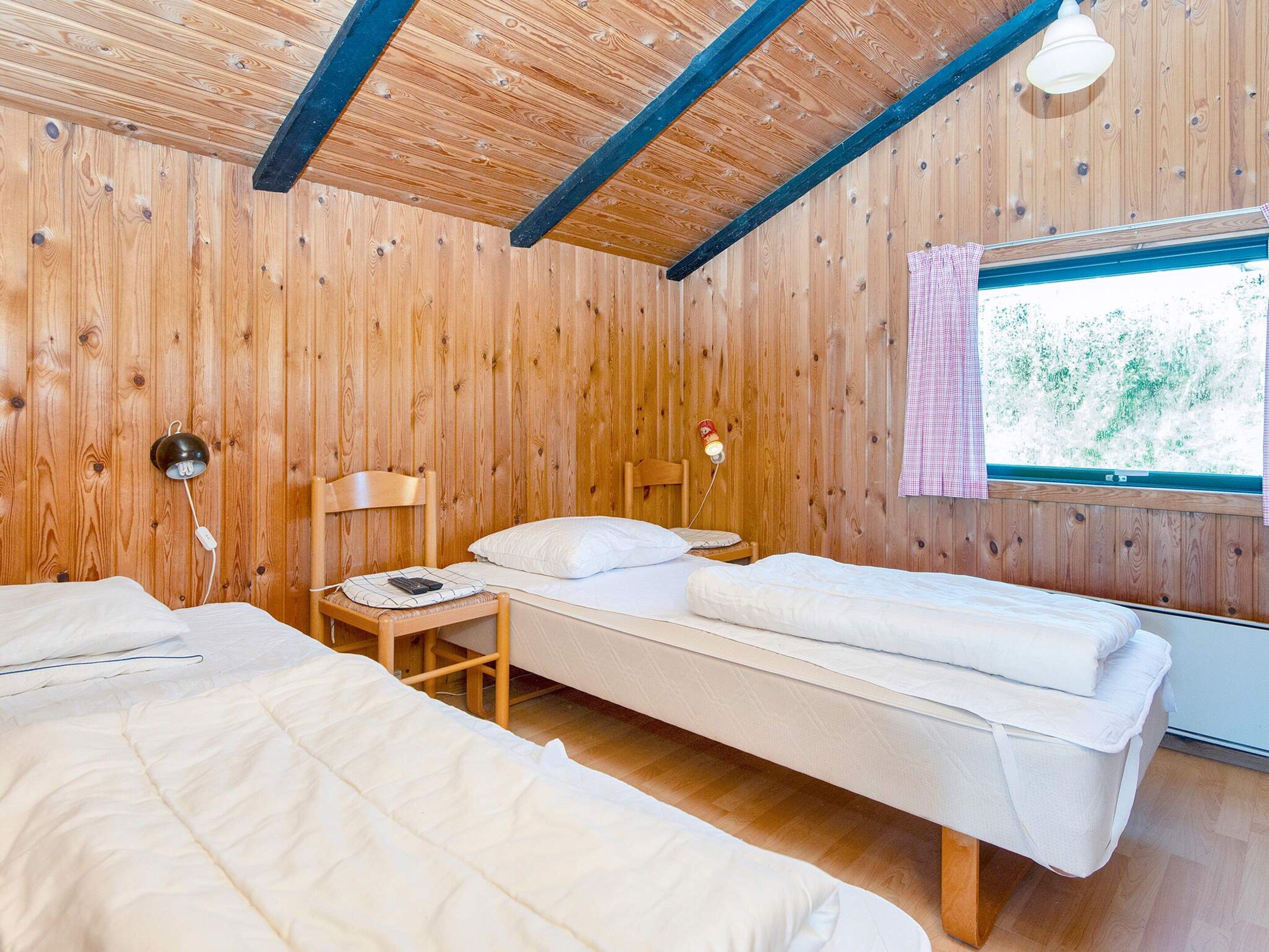 Une pièce aux murs en bois et au plafond en pente, comprenant deux lits, une petite table et une lampe.