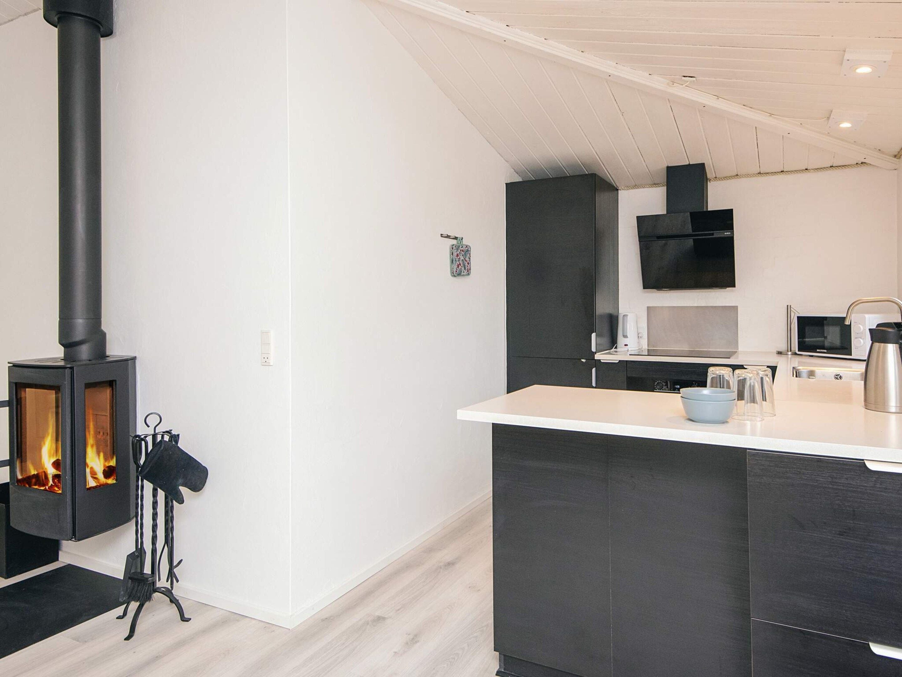A modern kitchen with a wood-burning stove, dark cabinetry, and a white countertop.