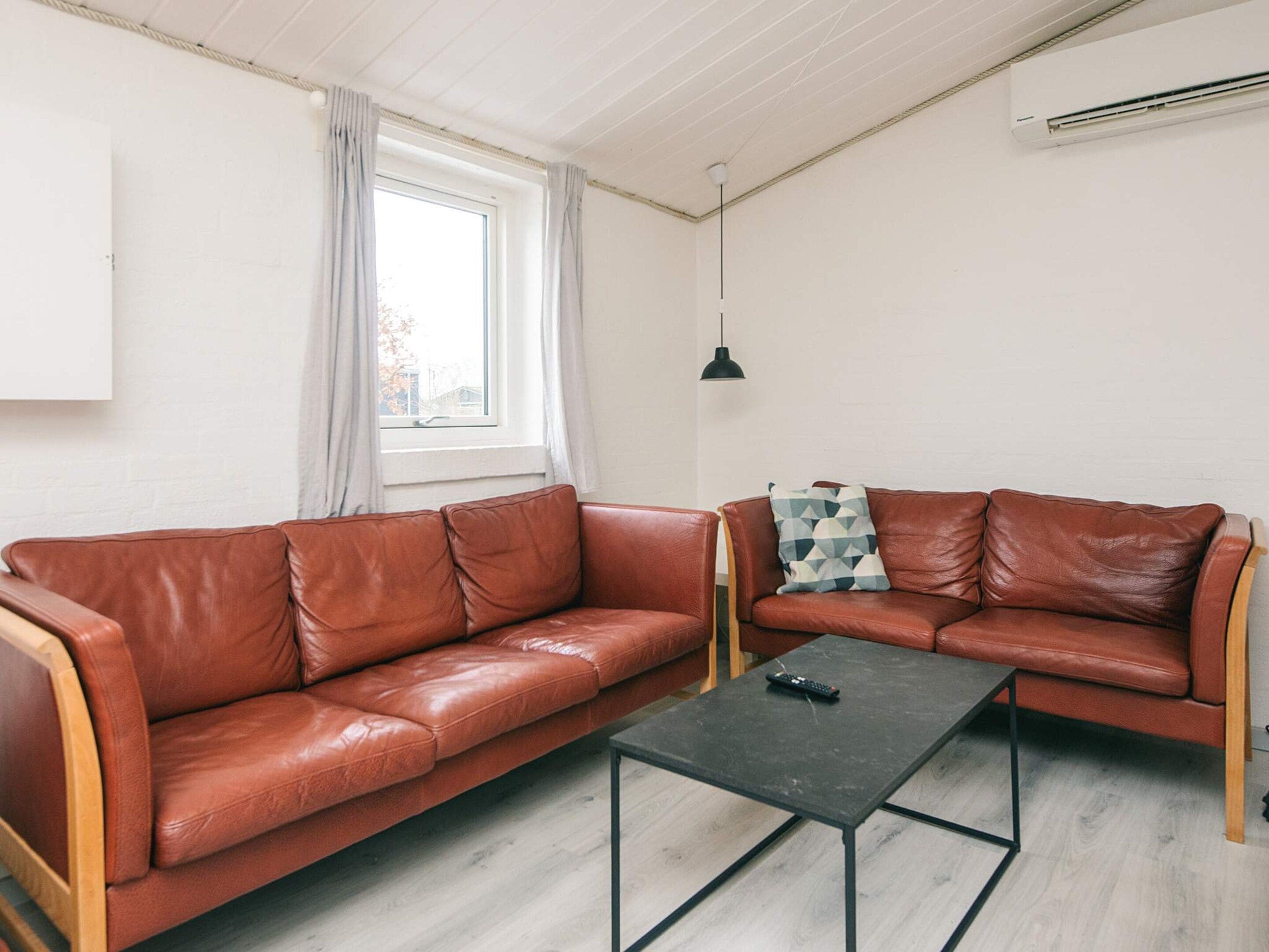 A modern living room with two leather sofas, a black coffee table, a window with curtains, a pendant light, and an air conditioning unit.