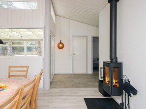 A room with a wood-burning stove, a dining table with chairs, and a view through a window. - 7 Person Holiday Home in Orsted (Ørsted)