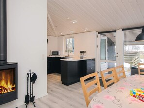 A modern kitchen with a central island, a dining area with wooden chairs, and a fireplace. - 7 Person Holiday Home in Orsted (Ørsted)