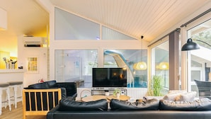 A modern living room with a large flat-screen TV, a sofa, and a dining area with a bar. - 4 Star Holiday Home in Saltum (Lokken)