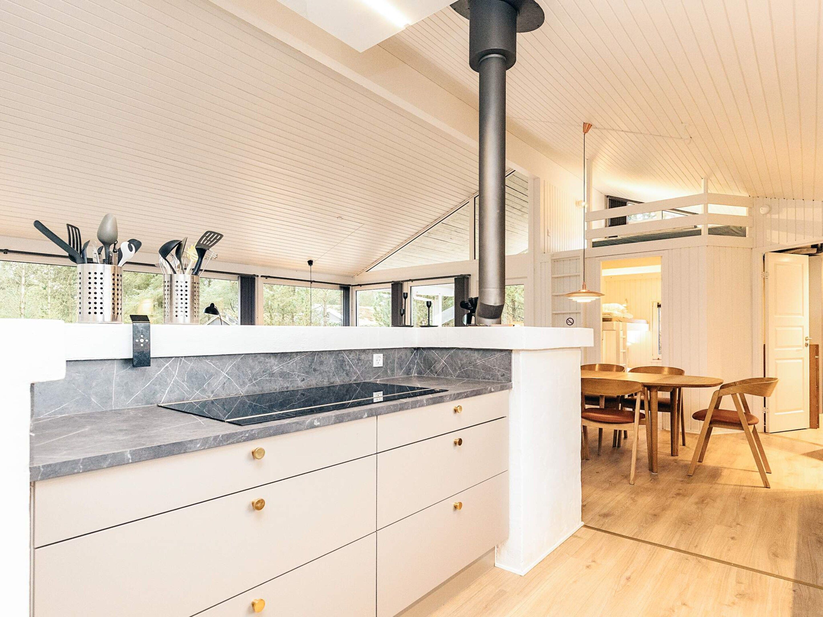 A modern kitchen with a large island, a black stove, and a dining area with wooden furniture.