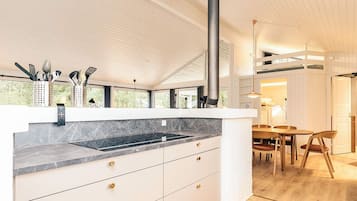 A modern kitchen with a large island, a black stove, and a dining area with wooden furniture.