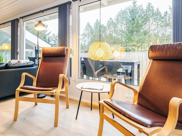 A modern living room with two leather chairs, a wooden coffee table, and a large window with a view of trees. - 4 Star Holiday Home in Saltum (Lokken)