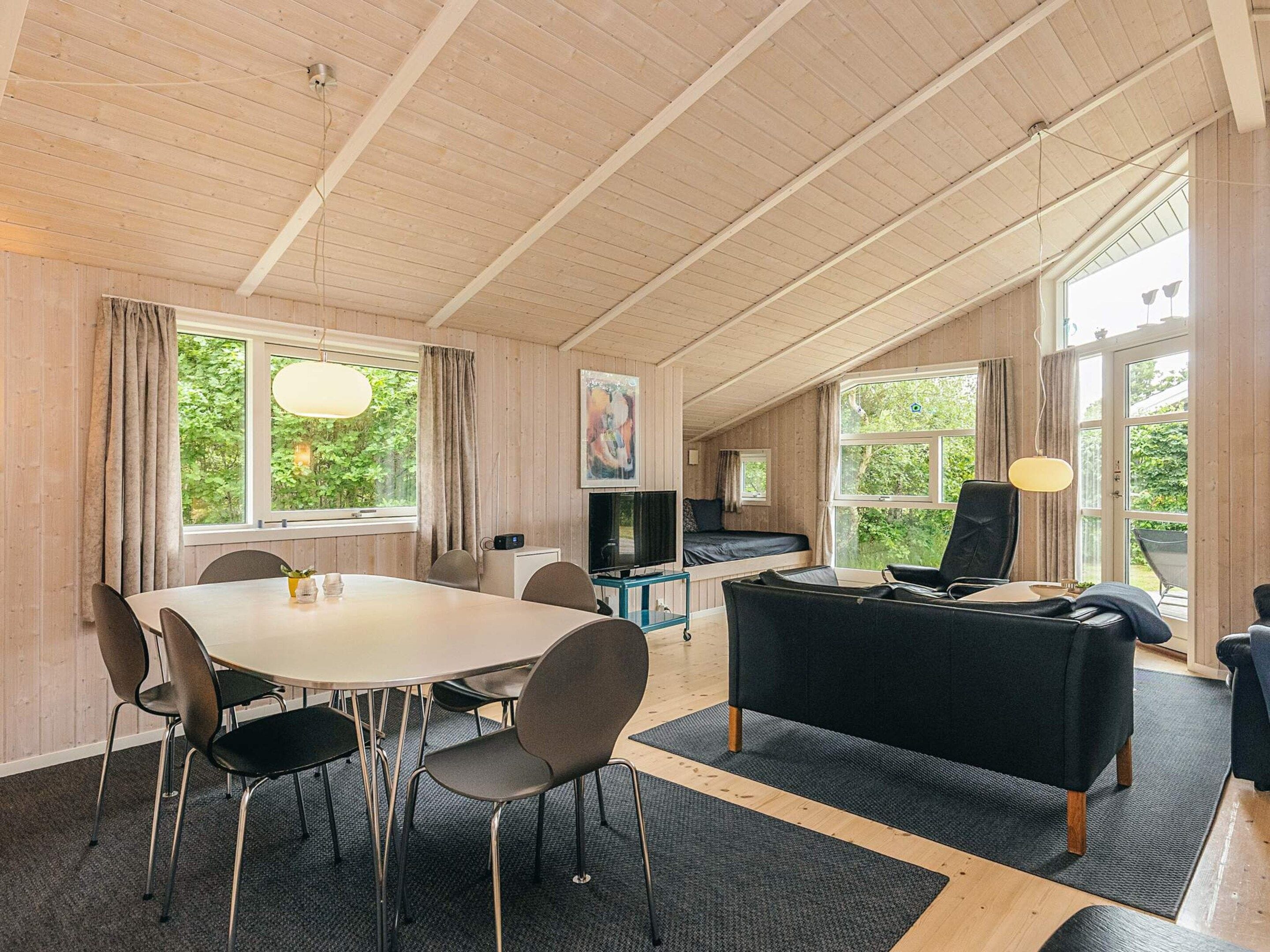 Ein Zimmer mit Esstisch, Stühlen, einer Couch, einem Fernseher und großen Fenstern.