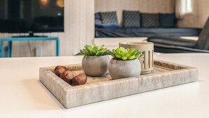 Ein modernes Wohnzimmer mit einer Couch, einem Couchtisch mit Topfpflanzen und Nüssen sowie einem Fernseher im Hintergrund.