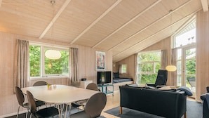 Ein geräumiges Zimmer mit Holzbalkendecke, einem Esstisch mit Stühlen, einem schwarzen Sofa und einem Fernseher.