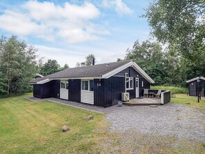 A single-story building with a dark exterior, a tiled roof, and a small porch area with a table and chairs. - 4 Star Holiday Home in Hadsund (Hadsund)