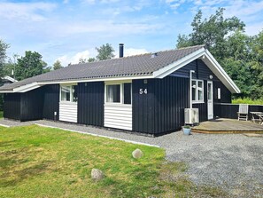 A black building with the number 54, a covered outdoor area with a table and chairs, and a grassy area in front. - 4 Star Holiday Home in Hadsund (Hadsund)
