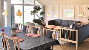 Uma sala de jantar moderna com uma mesa posta para quatro pessoas, rodeada por cadeiras de vime e um sofá.