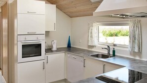 Uma cozinha moderna com armários brancos, forno embutido, lava-louças e uma janela grande com cortinas.