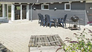 Uma casa com um pátio que inclui uma mesa, cadeiras, churrasqueira e um deck de madeira.