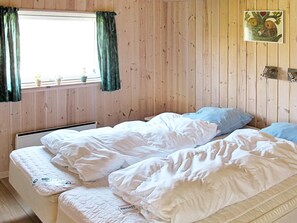 Ett rum med träpanel på väggarna, en säng med vita sängkläder, ett fönster med gröna gardiner och en liten växt på fönsterbrädan.