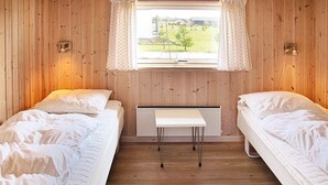 Quarto com duas camas de solteiro, uma mesinha e janela com cortinas.