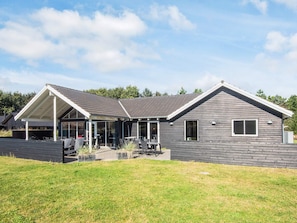 A modern house with a covered patio, large windows, and a well-maintained lawn. - Chic Holiday Home in Jutland near Sea (Blavand)