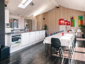 A modern kitchen with a central island, white cabinetry, and a dining area with a long table and chairs. - Chic Holiday Home in Jutland near Sea (Blavand)