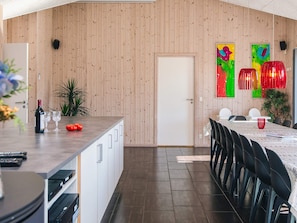 A modern kitchen with a wooden wall, a dining area with a long table and chairs, and a door leading to another room. - Chic Holiday Home in Jutland near Sea (Blavand)