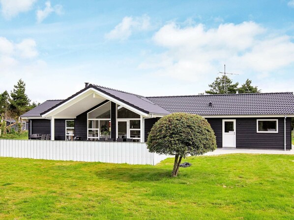 A modern two-story house with a covered patio, a fenced yard, and a well-maintained lawn.