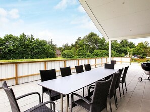 An outdoor patio with a table and chairs, a barbecue grill, and a view of a house and trees.