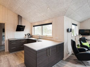 Et moderne køkken med mørke skabe, en stor ø og en indbygget ovn. Der er et vindue med udsigt til grøn bevoksning.
