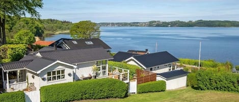 A residential area with houses, a well-maintained lawn, and a large body of water in the background.