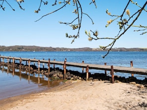 Un muelle de madera se extiende sobre aguas tranquilas, rodeado de rocas y una playa arenosa.