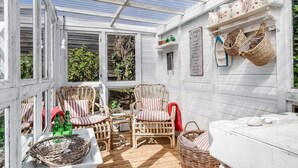 A covered outdoor seating area with wicker furniture and a white table, surrounded by white walls and a glass roof. - 4 Star Holiday Home in Borkop (Borkop)