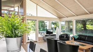 A spacious indoor area with a large potted plant, black leather furniture, and a television. - 4 Star Holiday Home in Hjorring (Hjørring)