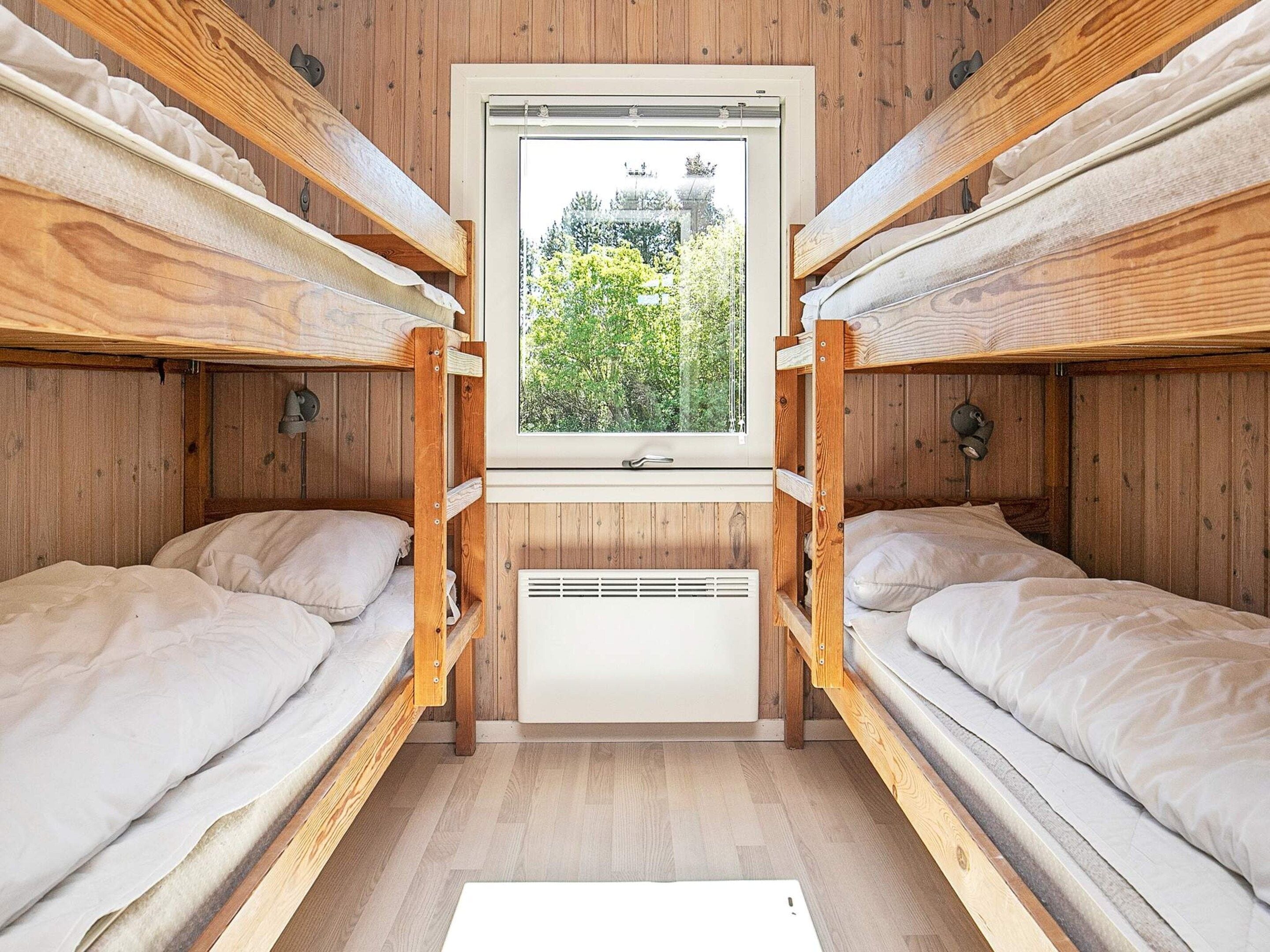 A bunk bed room with a window, wooden walls, and a white radiator.