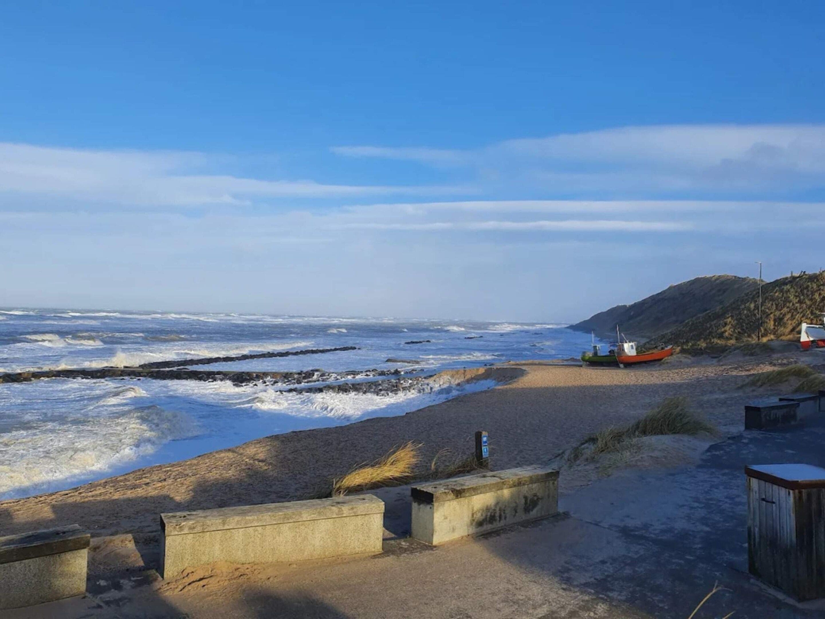 A beach with waves, a boat, and a rocky hill.