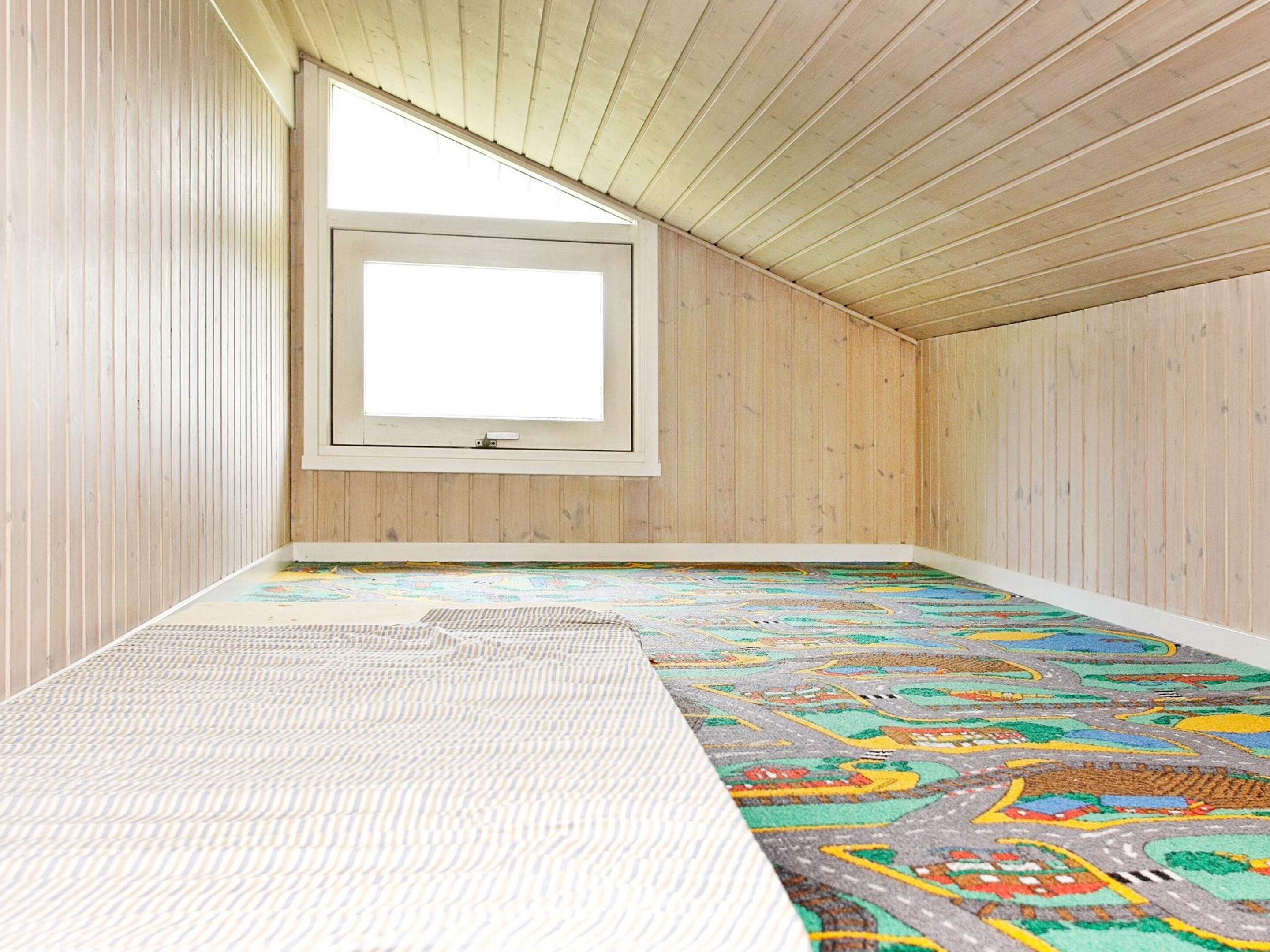 A room with a sloped ceiling, wooden walls, a window, and a colorful carpet.