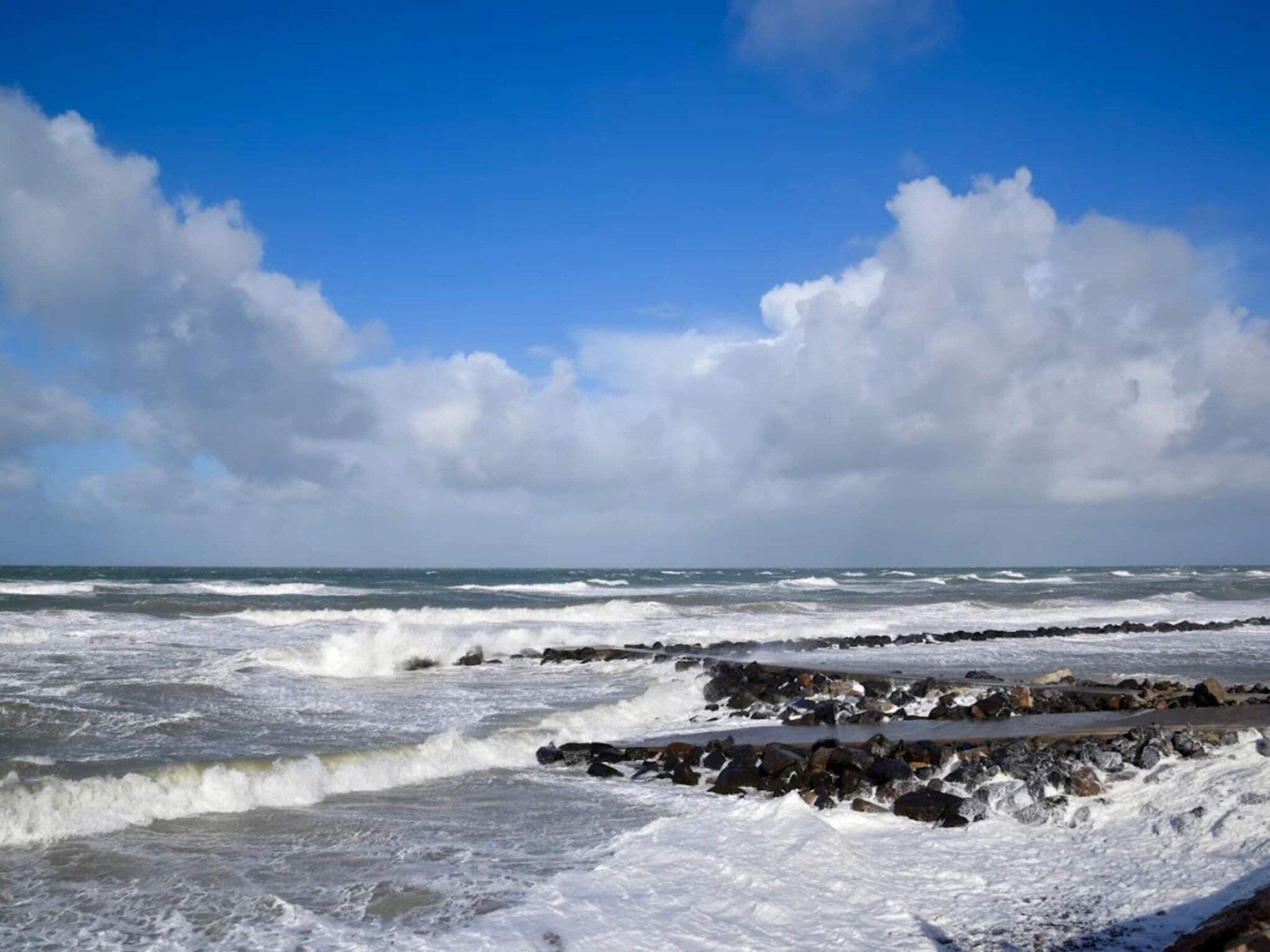 A coastal scene with waves crashing against a rocky shore under a partly cloudy sky.