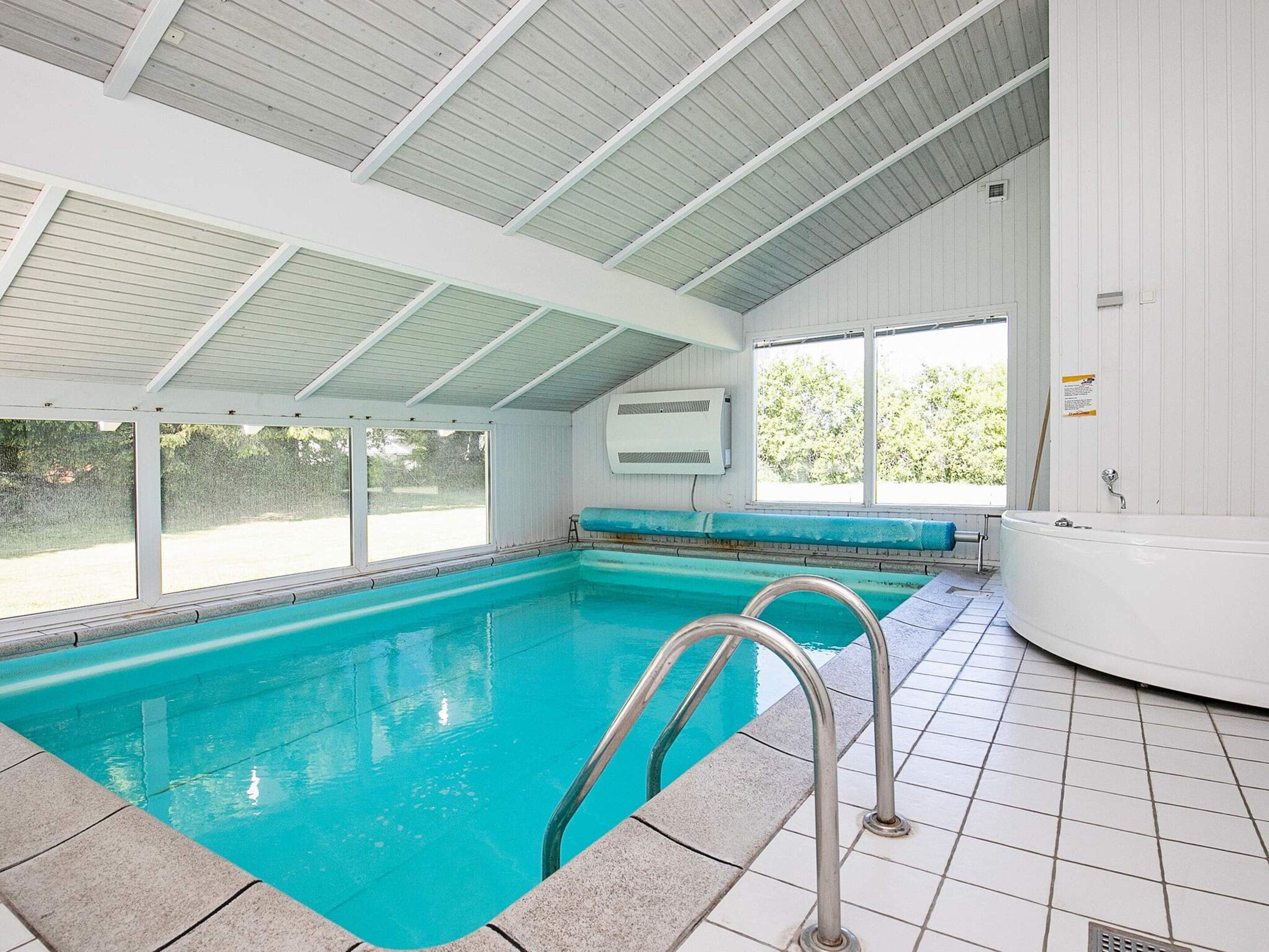 An indoor swimming pool with clear water, a diving board, and a hot tub.