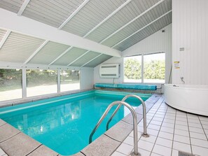 An indoor swimming pool with clear water, a diving board, and a hot tub.