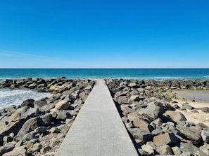 A concrete pathway leading to a rocky shoreline with the ocean in the background.