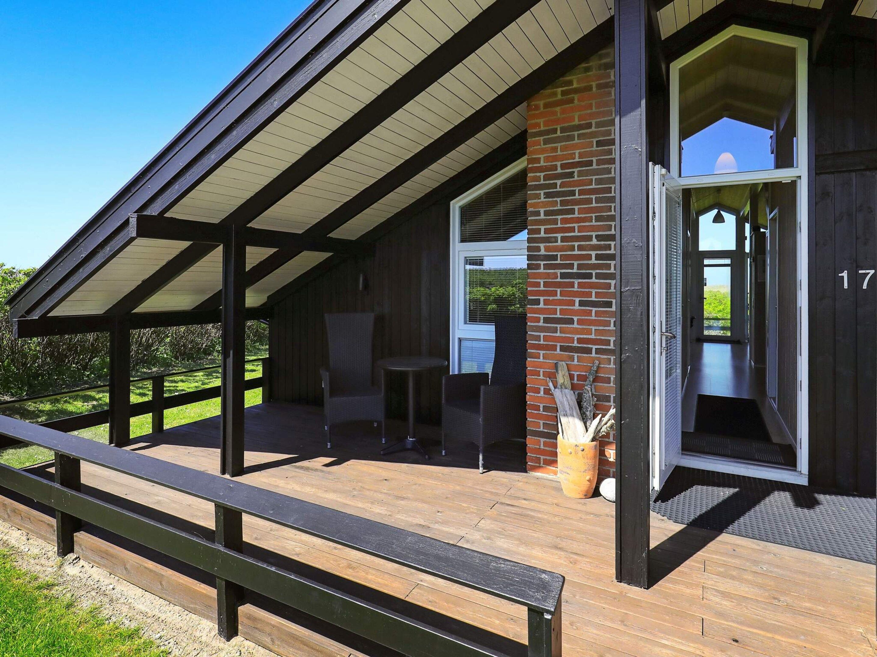 Un espace extérieur abrité doté d’une terrasse en bois, d’un mur en briques et d’une porte donnant accès à un espace intérieur.