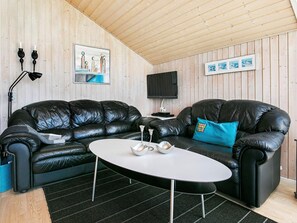 A room with a black leather sofa, a white coffee table, a TV mounted on the wall, and wooden paneling. - 4 Star Holiday Home in Lokken (Lokken)