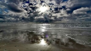 Ein Strand mit Wellen, bewölktem Himmel und Sonnenschein.