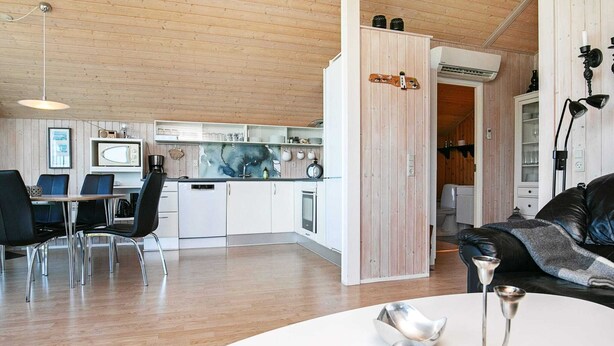 Eine moderne Küche mit weißen Schränken, ein Essbereich mit einem weißen Tisch und Stühlen sowie ein Wohnbereich mit einem schwarzen Ledersofa.