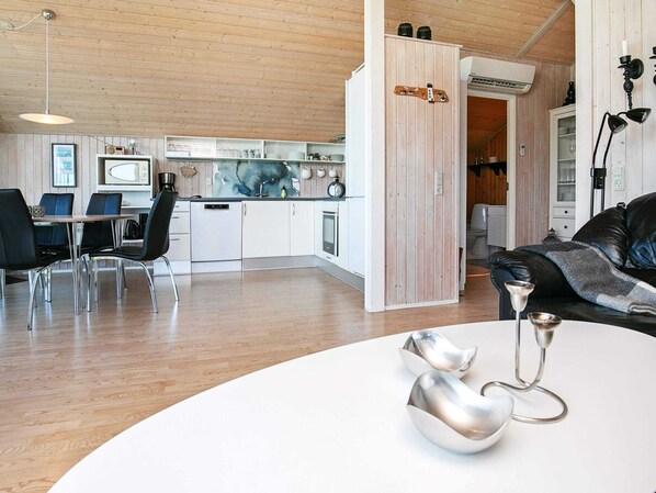 Eine moderne Küche mit weißen Schränken, ein Essbereich mit einem weißen Tisch und Stühlen sowie ein Wohnbereich mit einem schwarzen Ledersofa.