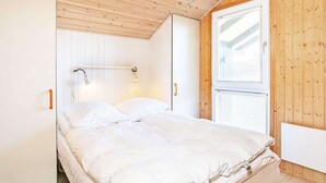 Ein Schlafzimmer mit Holzbalkendecke, einem Bett mit weißer Bettwäsche, einer Nachttischlampe und einem Fenster mit Jalousien.