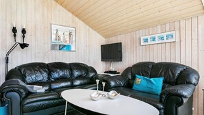 Ein gemütliches Wohnzimmer mit einer schwarzen Ledersofa, einem kleinen weißen Tisch und einem an der Wand befestigten Fernseher.